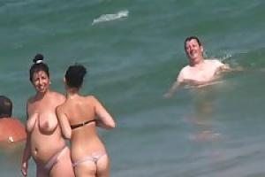 Обнаженные женщины наслаждаются на пляже в то время как парни смотрят на их гладко выбритыми кисками